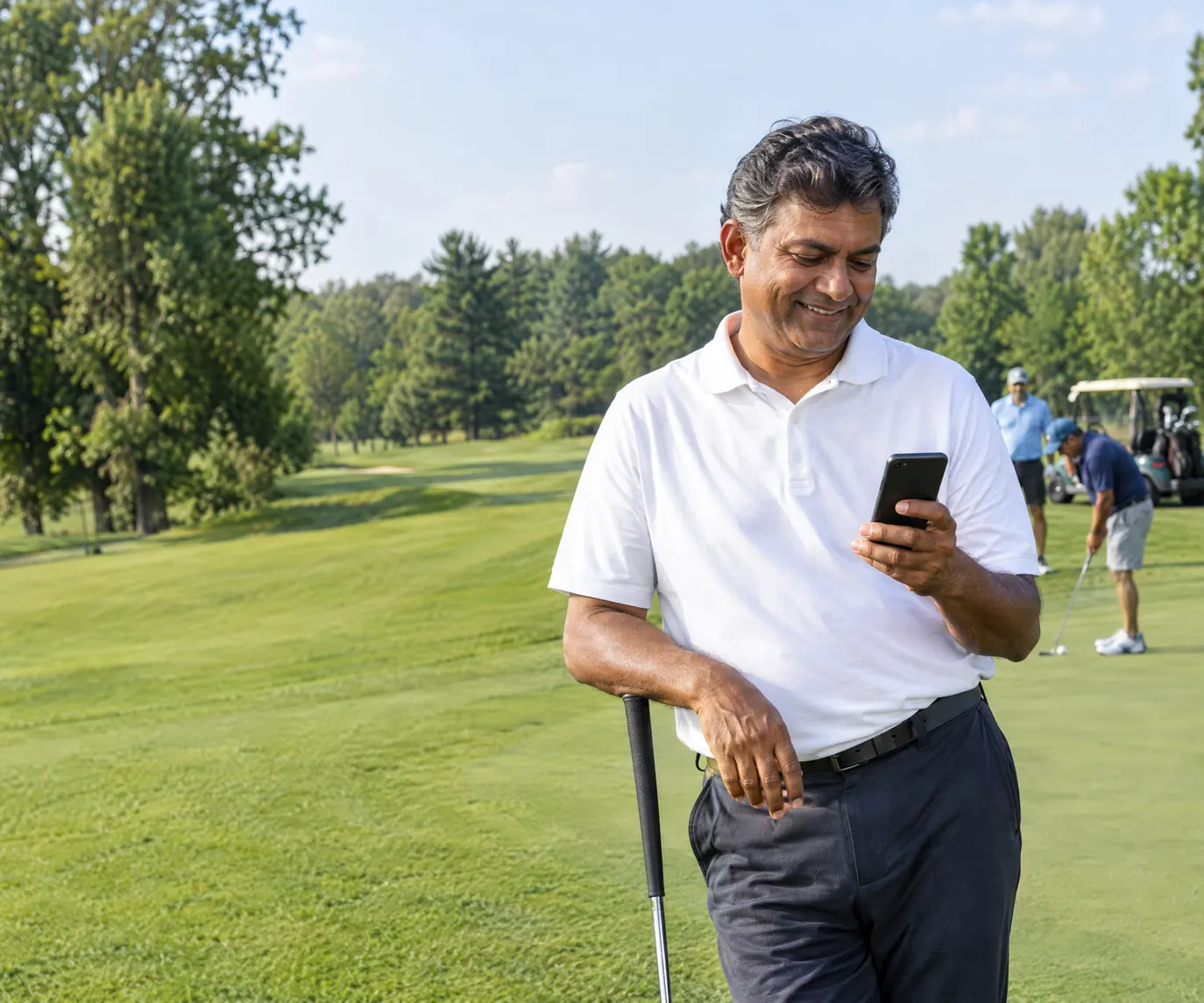 A rental operator on a golf course glancing at his phone while friends putt behind him