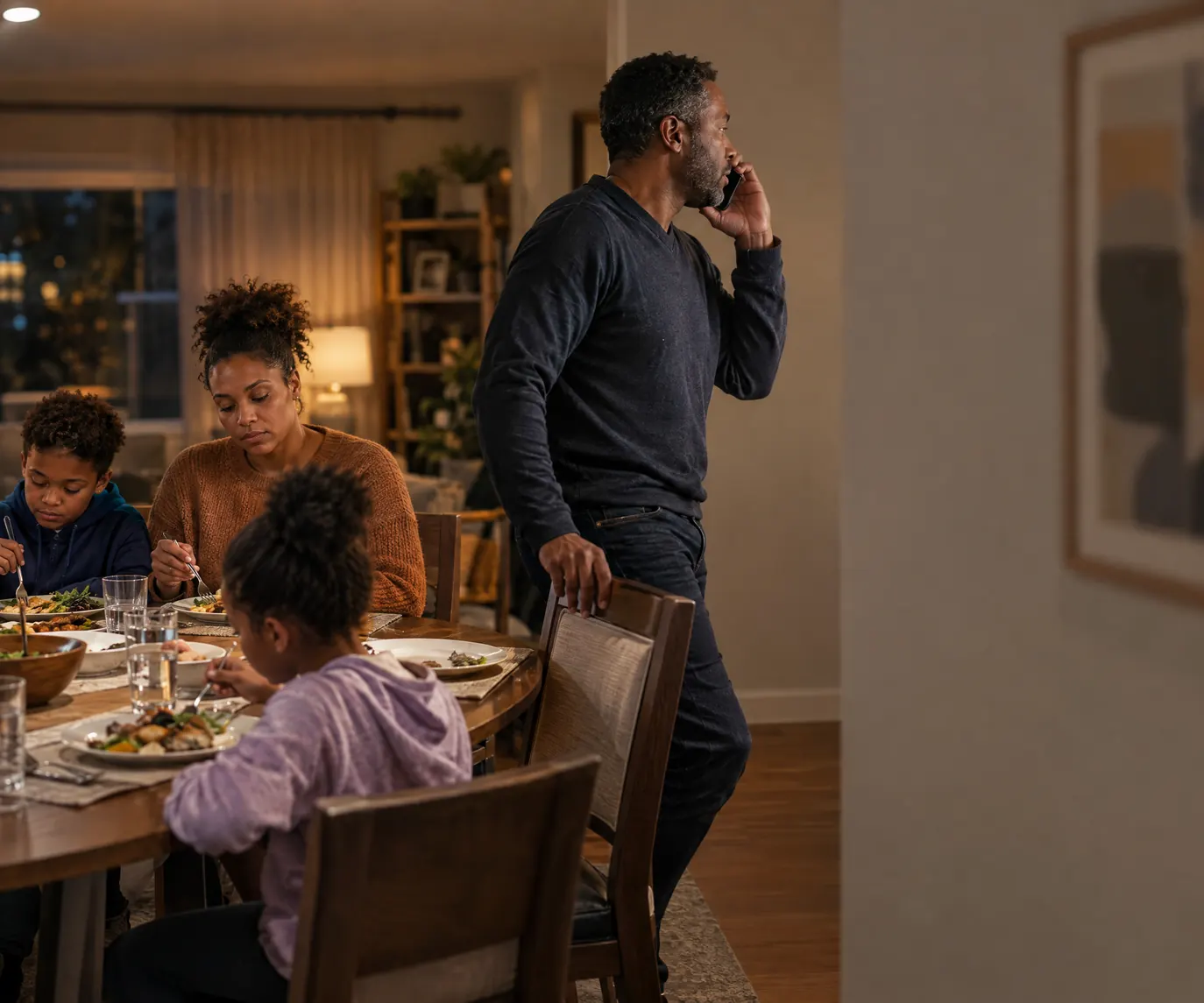 A rental operator standing up from family dinner to take a call while his family keeps eating