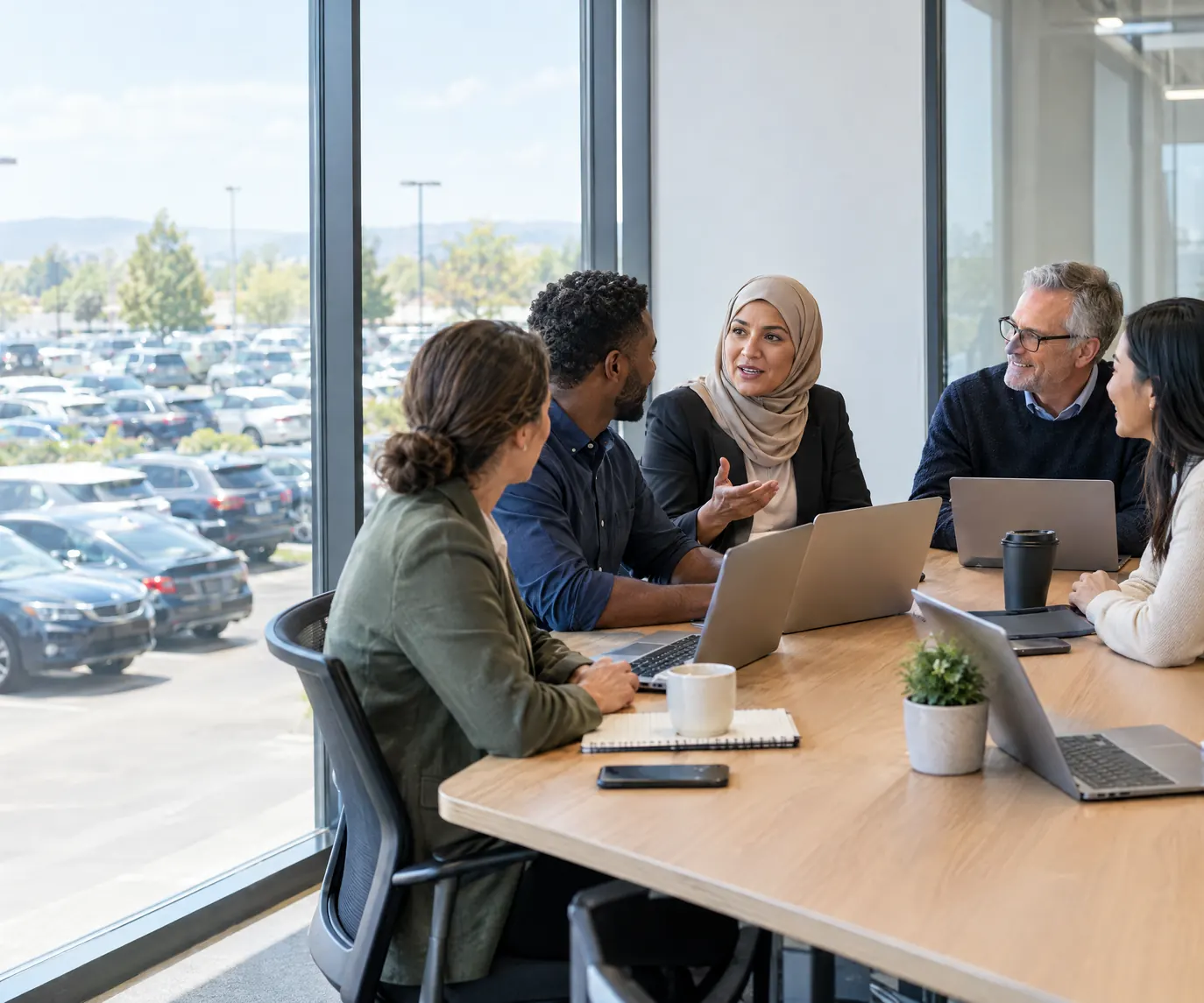 A rental company operations team in a weekly review, laptops open, the lot outside the glass wall